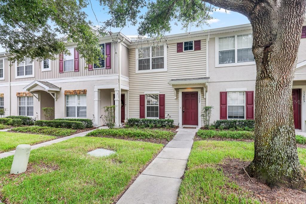 A row of two-story townhouses with beige siding, red shutters, and a front walkway — 15807 FISHHAWK FALLS DRIVE, LITHIA, FL