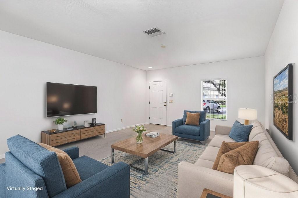 A living room with a wall-mounted television, blue armchairs, a sofa, and a coffee table — 15807 FISHHAWK FALLS DRIVE, LITHIA, FL