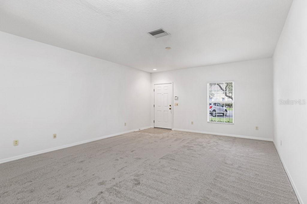 An empty room with white walls, gray carpeting, a front door, and a window — 15807 FISHHAWK FALLS DRIVE, LITHIA, FL