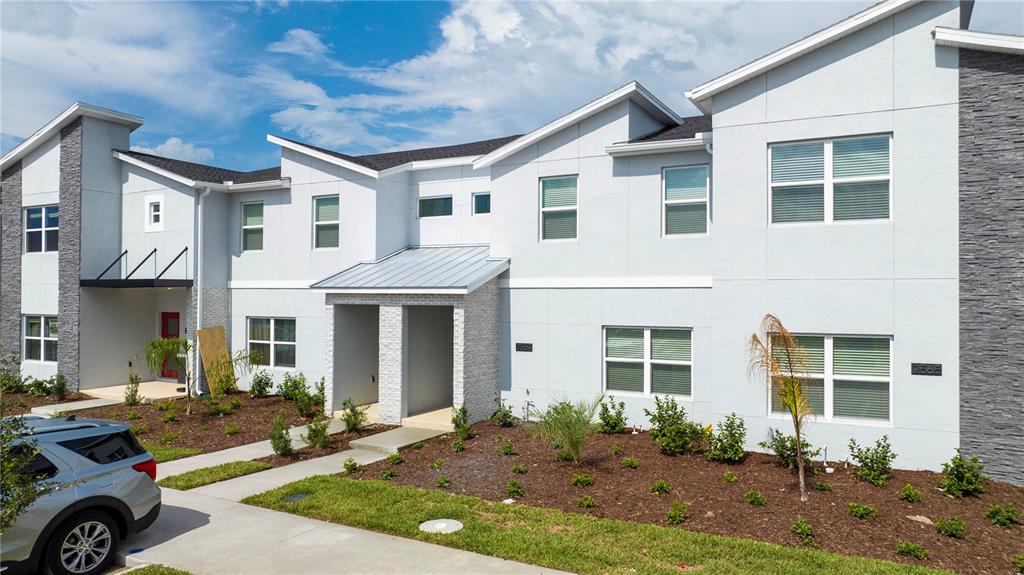 A two-story townhouse exterior features light gray siding, stone accents, and a metal roof entryway — 2569 READING TRAIL, KISSIMMEE, FL