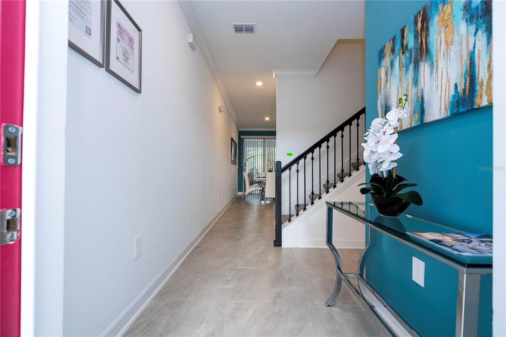 A hallway with tile flooring leads past a staircase to a dining area — 2569 READING TRAIL, KISSIMMEE, FL
