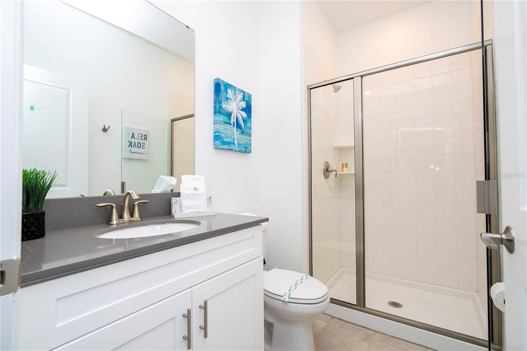 A bathroom features a white vanity with a gray countertop, a toilet, and a glass-enclosed shower — 2569 READING TRAIL, KISSIMMEE, FL