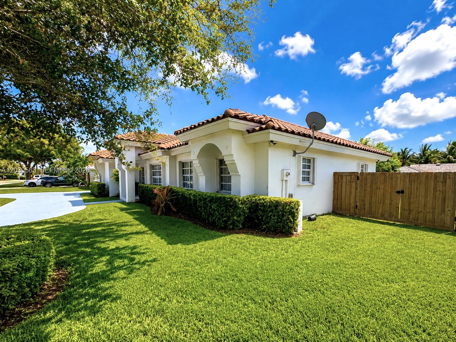 A white single-story house with a tile roof, green lawn, and a wooden privacy fence — 15690 SW 153rd Ct, Miami FL 33187, MIAMI, FL