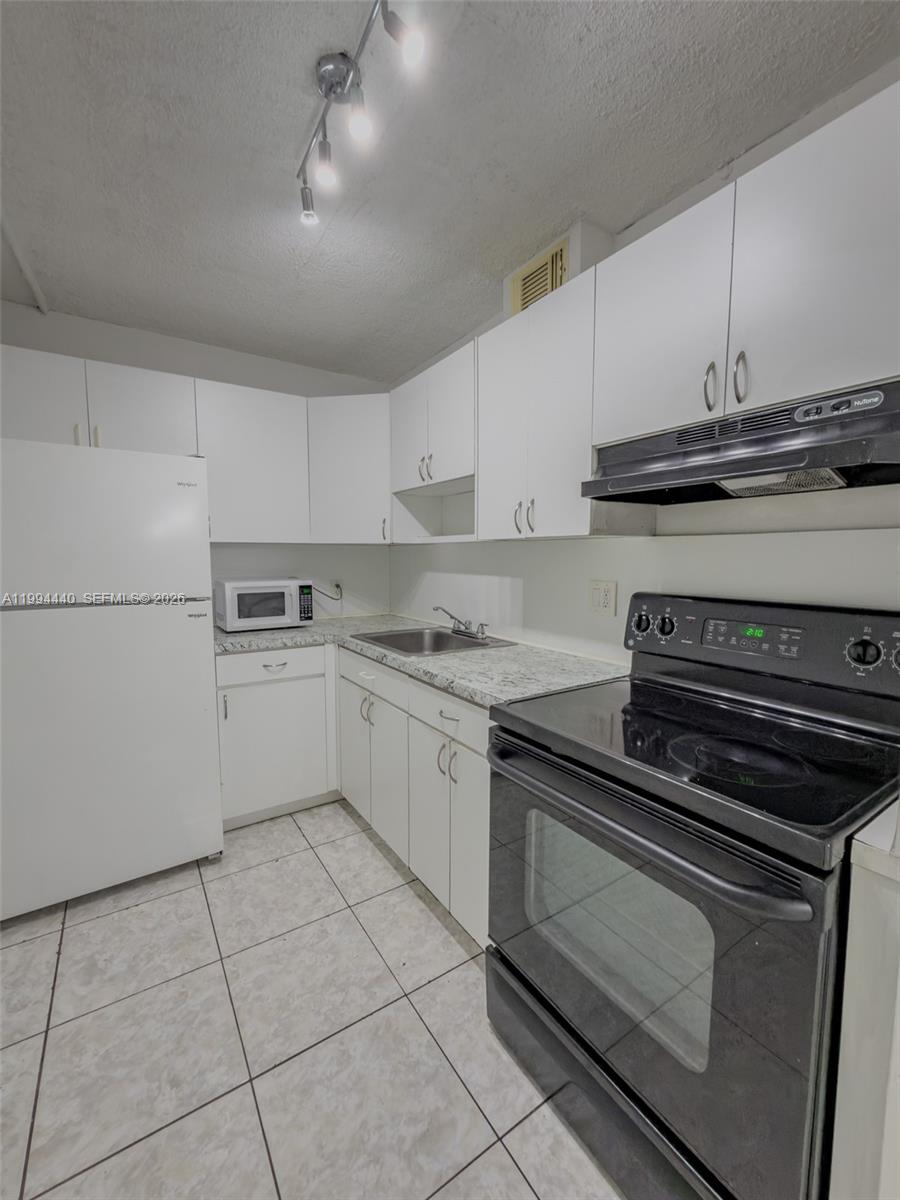 A kitchen features white cabinets, a black stove, a white refrigerator, and light-colored tile flooring — 8411 NW 8th St # 301, Miami FL 33126, MIAMI, FL