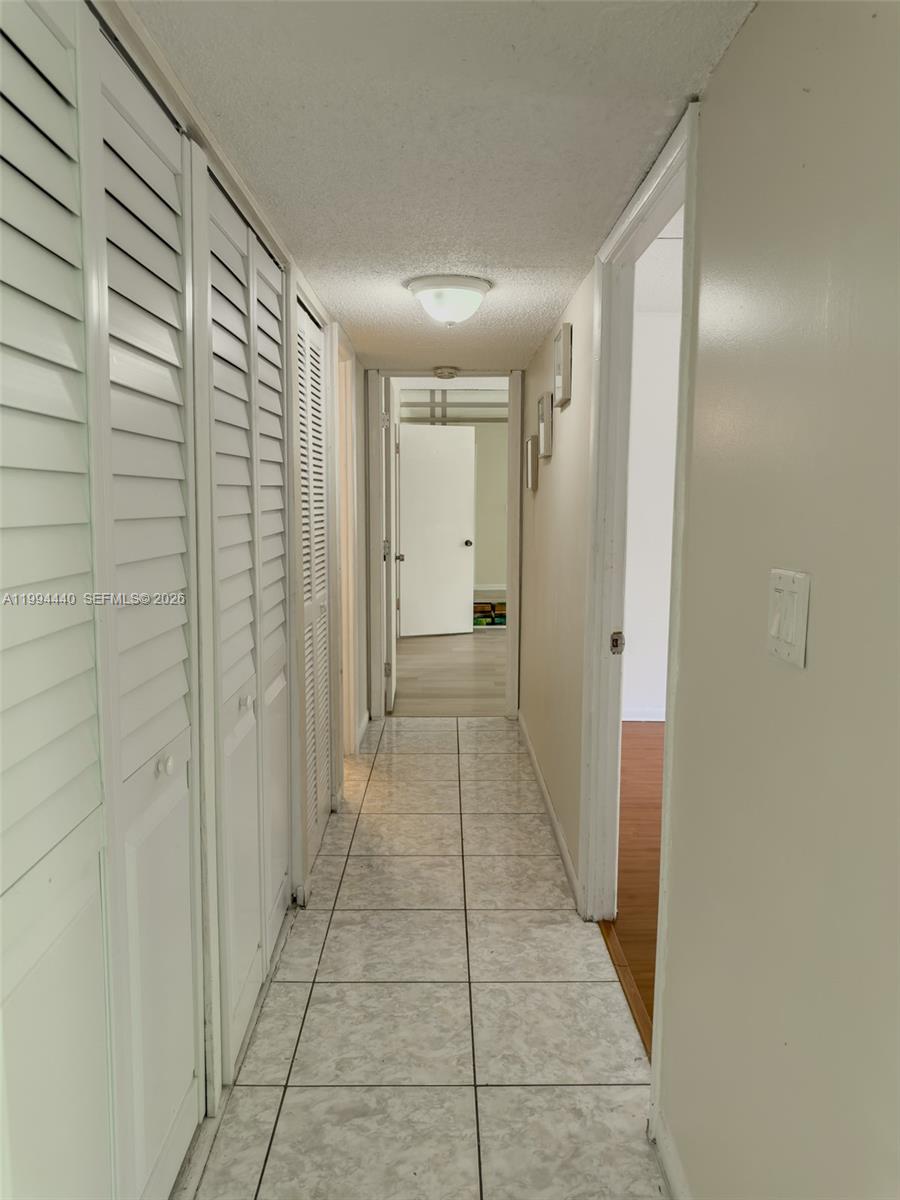 A hallway with white louvered closet doors, tiled floors, and a light fixture — 8411 NW 8th St # 301, Miami FL 33126, MIAMI, FL