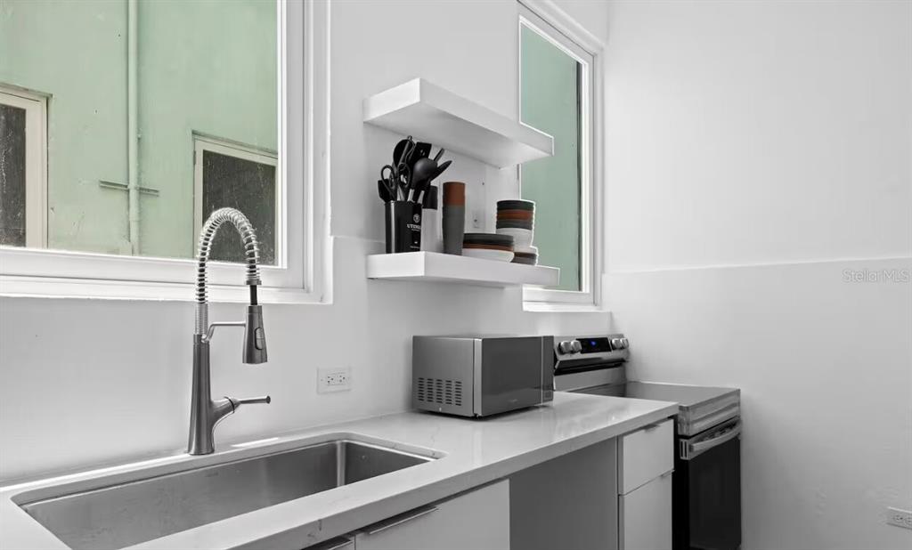 A kitchen features a stainless steel sink, white countertops, floating shelves, and a microwave — 250 CALLE DEL PARQUE UNIT 3A, SAN JUAN, PR