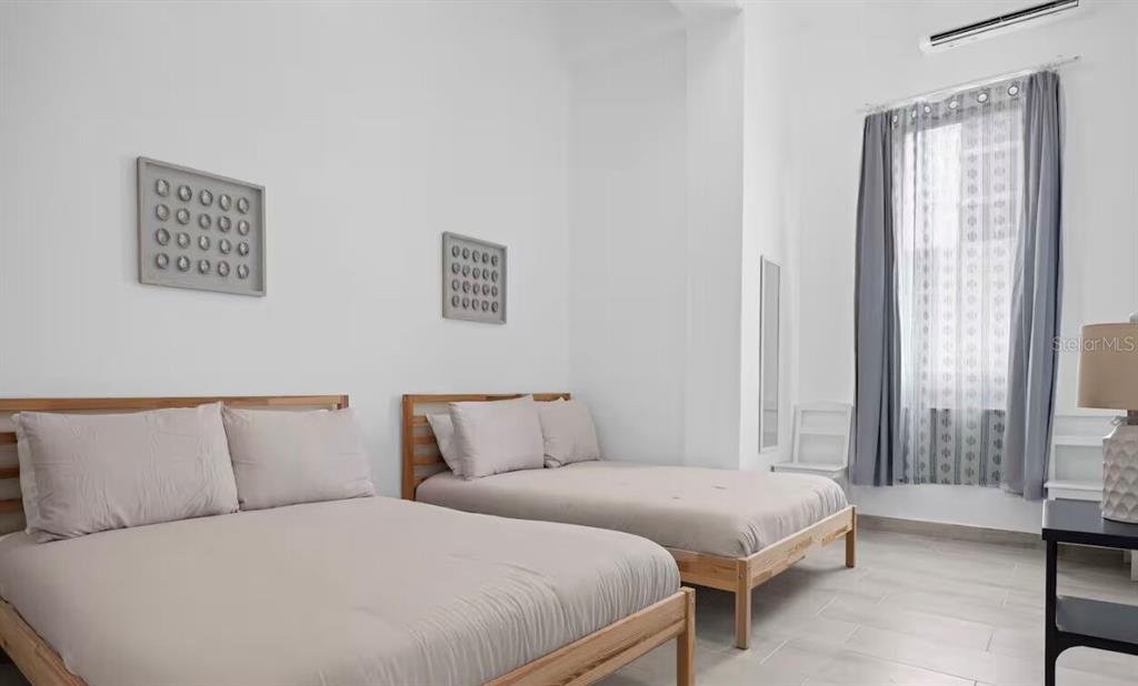 A bedroom features two beds with light-colored bedding, white walls, and a window with curtains — 250 CALLE DEL PARQUE UNIT 3A, SAN JUAN, PR