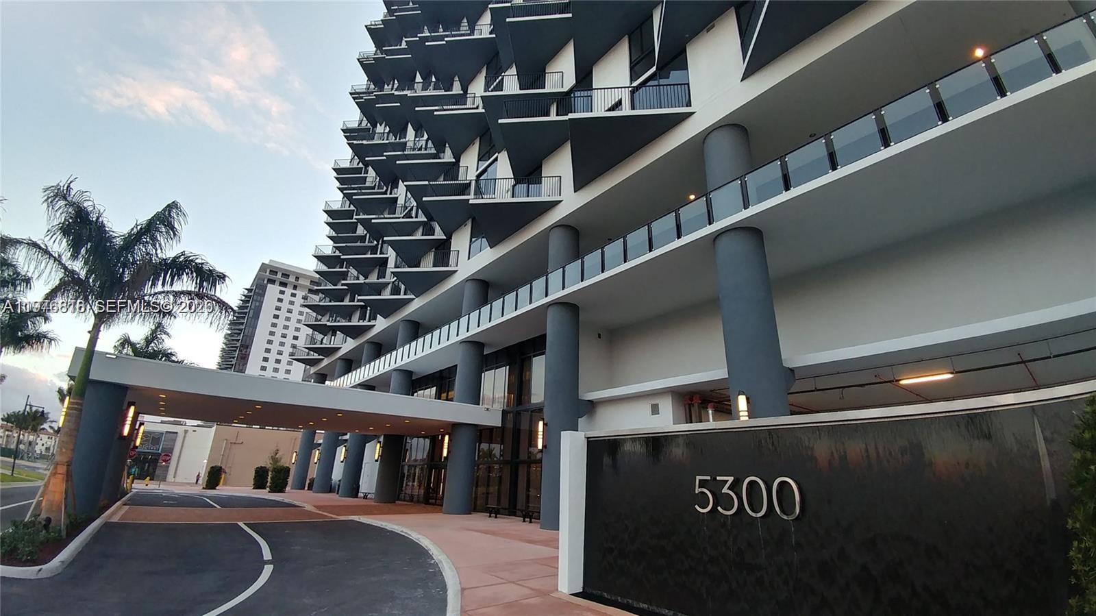 A low-angle exterior view shows a modern high-rise building with balconies and a driveway — 5300 PASEO BLVD # 1603, Doral FL 33166, DORAL, FL