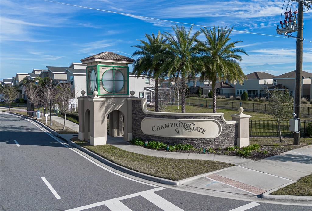 An exterior view of the ChampionsGate community entrance sign with palm trees and residential homes — 1435 OLYMPIC CLUB BOULEVARD, CHAMPIONS GATE, FL