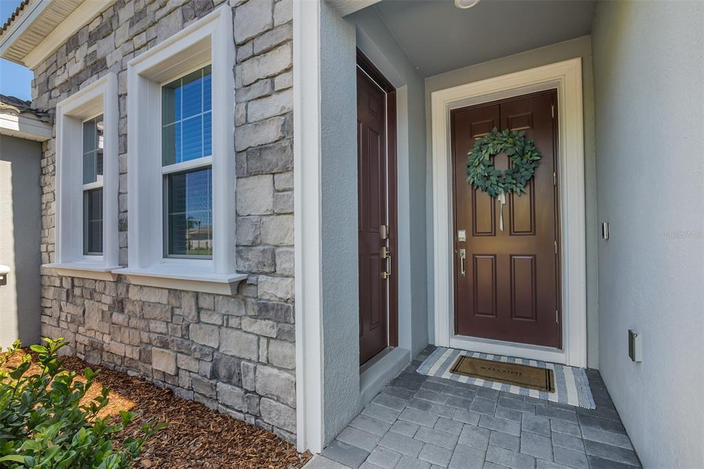 A stone-faced house exterior features a brown front door with a wreath and a doormat — 1435 OLYMPIC CLUB BOULEVARD, CHAMPIONS GATE, FL