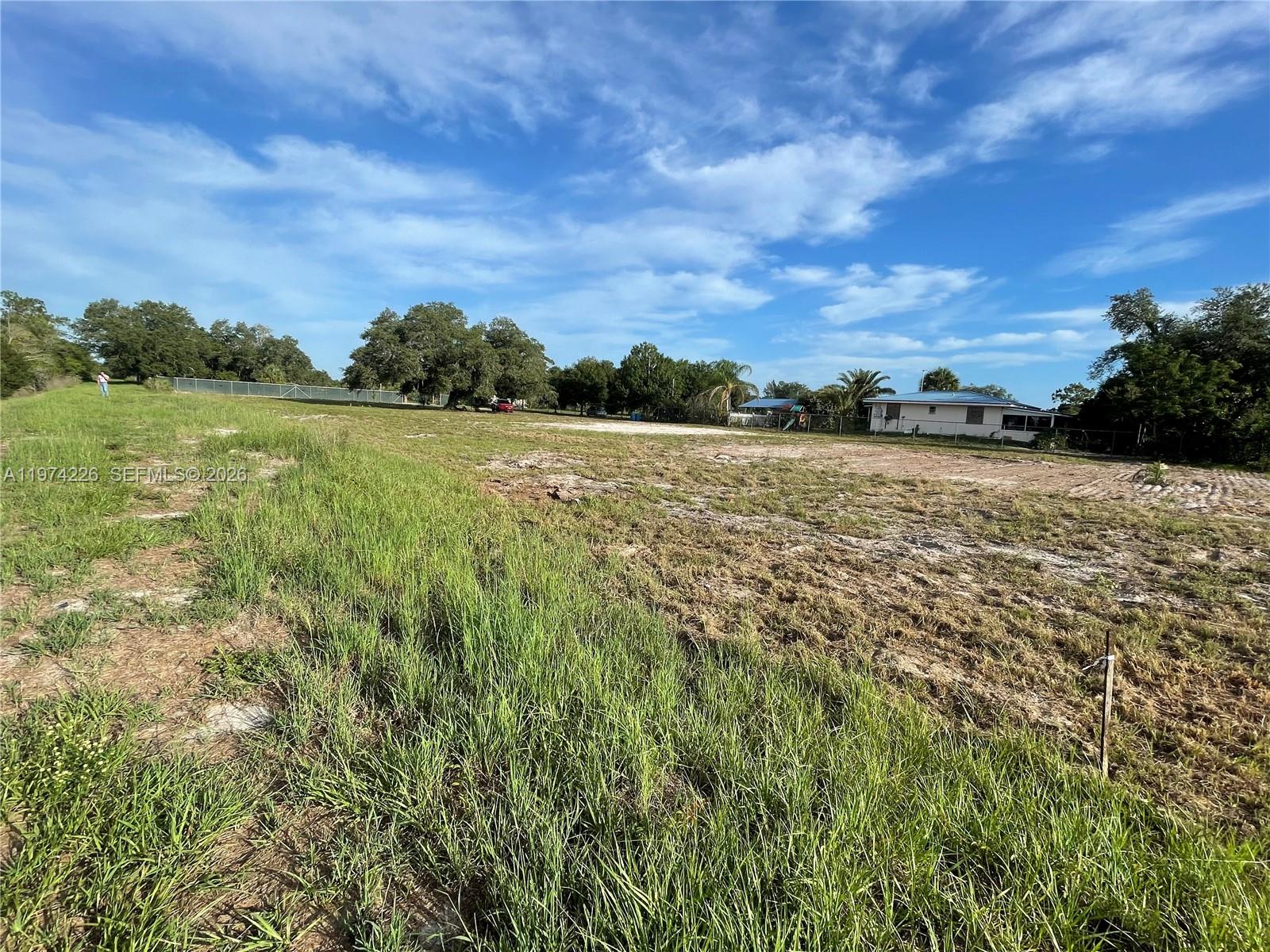 A large, cleared grassy lot features a house in the background under a blue sky — 615 N Brida Street, Clewiston FL 33440, CLEWISTON, FL