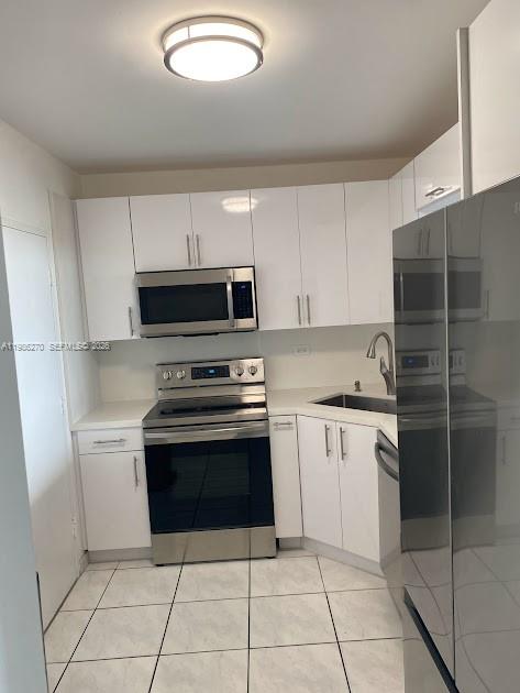 A kitchen features white cabinets, stainless steel appliances, and light-colored tiled flooring — 5601 Collins Ave # 1524, Miami Beach FL 33140, MIAMI BEACH, FL