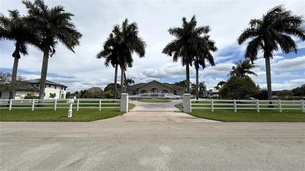 A gated driveway leads to a single-story house surrounded by palm trees and white fencing — 4810 SW 198 TERRACE, SOUTHWEST RANCHES, FL