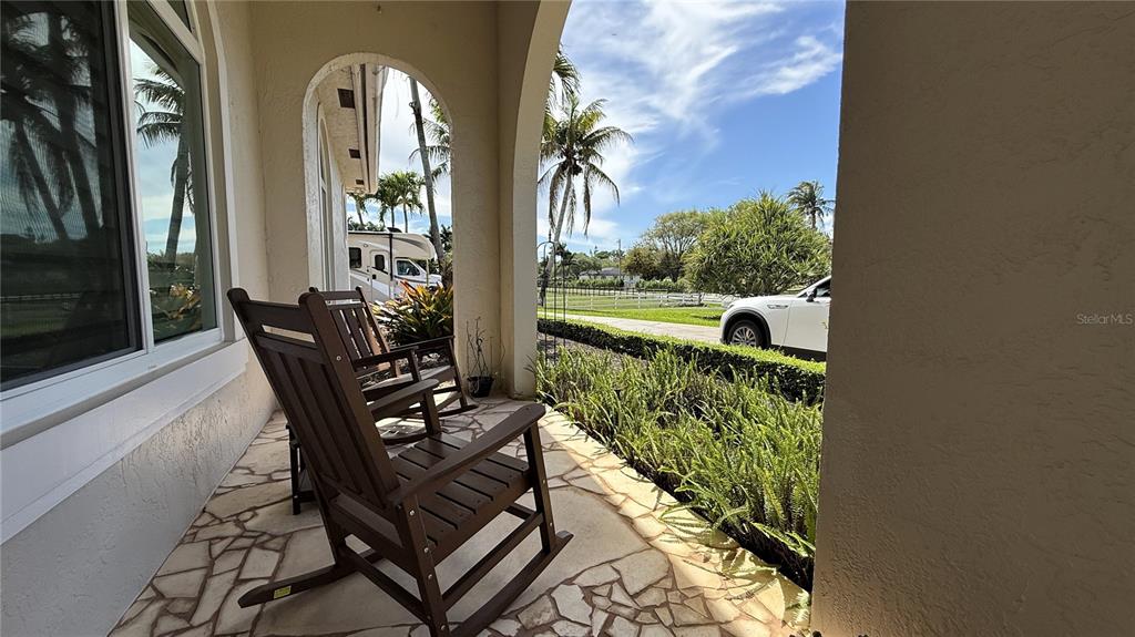 A covered porch features two wooden rocking chairs on a stone floor overlooking a yard — 4810 SW 198 TERRACE, SOUTHWEST RANCHES, FL