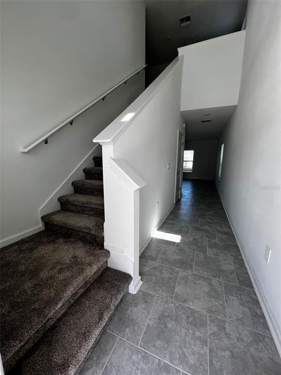 A staircase with brown carpet leads upward next to a tiled hallway — 433 SANDBAR LANE, HAINES CITY, FL