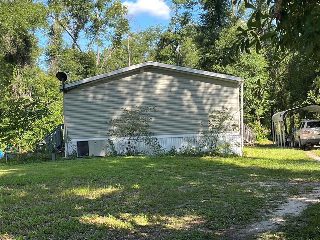 The exterior of a light-colored manufactured home features vinyl siding, dark shutters, and a wooden porch — 10452 COUNTY ROAD 136, LIVE OAK, FL