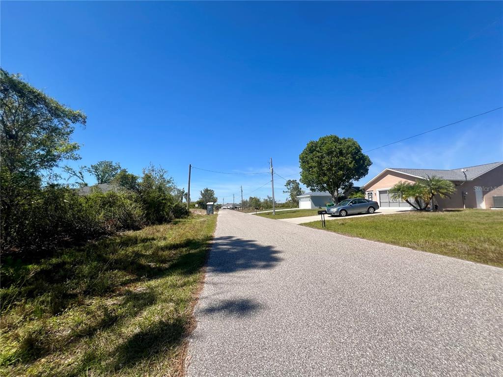 A paved residential street stretches past a house with a car parked in the driveway — 5129 RILKE LANE, PORT CHARLOTTE, FL