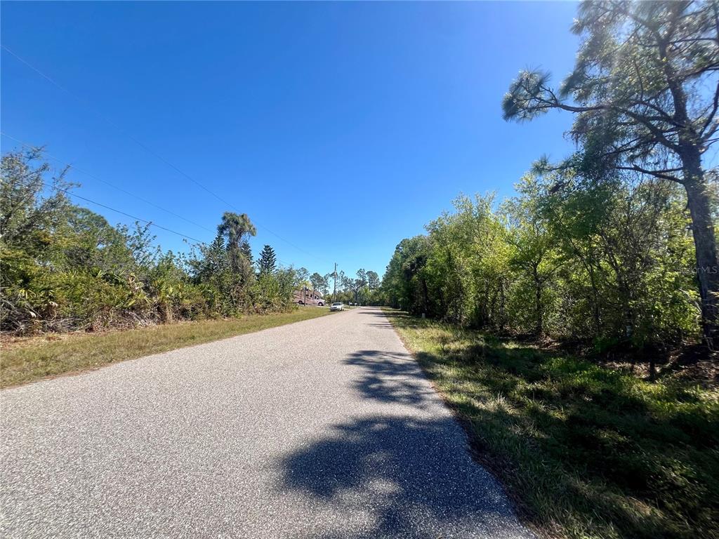 A paved road stretches between wooded lots under a clear blue sky — 5129 RILKE LANE, PORT CHARLOTTE, FL