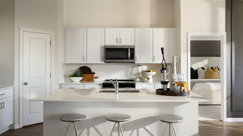 A kitchen features white cabinets, a central island with bar stools, and stainless steel appliances — 9249 ORCHARD PARK LANE, DADE CITY, FL
