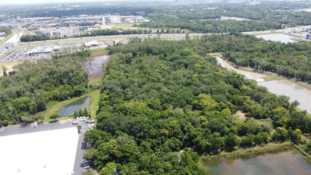 An aerial view shows a dense wooded lot surrounded by commercial buildings and retention ponds — 3604 W NEW HAMPSHIRE STREET, ORLANDO, FL