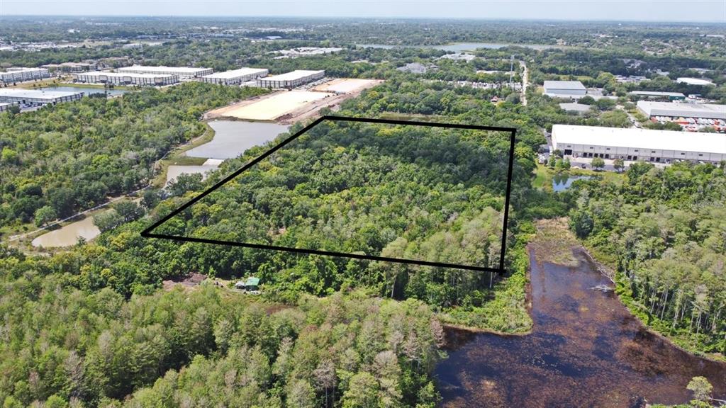 An aerial view shows a rectangular plot of wooded land outlined in black near warehouses — 3604 W NEW HAMPSHIRE STREET, ORLANDO, FL