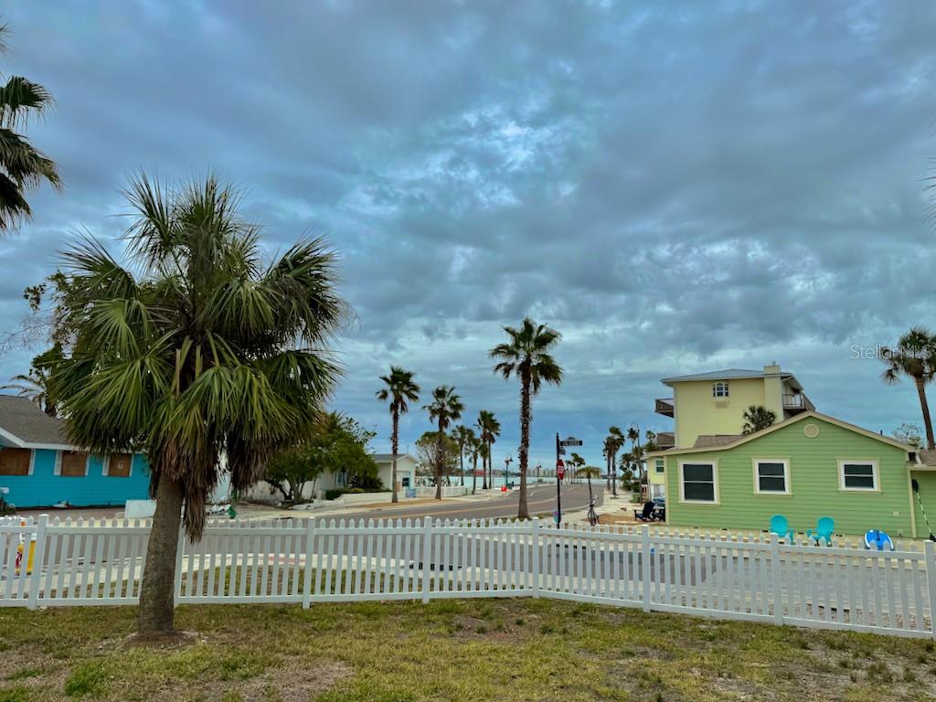 A white fence surrounds a yard with palm trees near a road and coastal houses — 1300 PASS A GRILLE WAY, ST PETE BEACH, FL