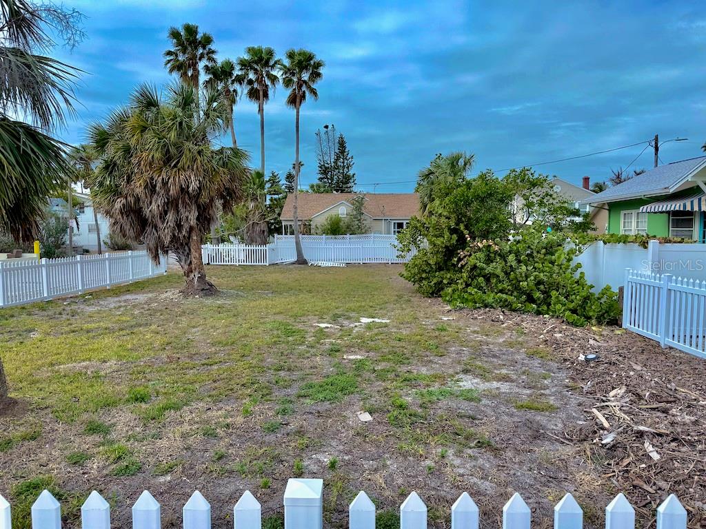 A fenced, grassy vacant lot features several palm trees under a cloudy blue sky — 1300 PASS A GRILLE WAY, ST PETE BEACH, FL