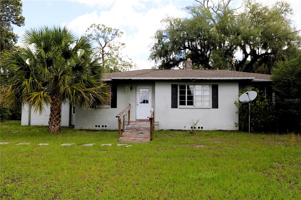 A single-story, light-colored brick house features a front wooden ramp and a large palm tree — 21514 SE 69TH AVENUE, HAWTHORNE, FL