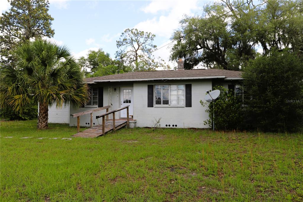 A single-story, light-colored brick house features a wooden wheelchair ramp leading to the front door — 21514 SE 69TH AVENUE, HAWTHORNE, FL
