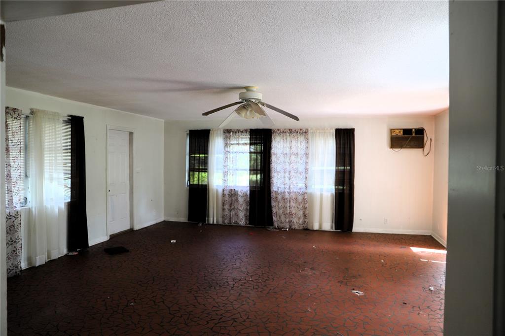 An empty living room features a ceiling fan, patterned flooring, and layered window curtains — 21514 SE 69TH AVENUE, HAWTHORNE, FL