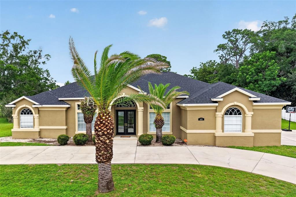 A single-story tan house with a dark roof, arched windows, and a paved driveway — 485 NW 45TH LANE, OCALA, FL