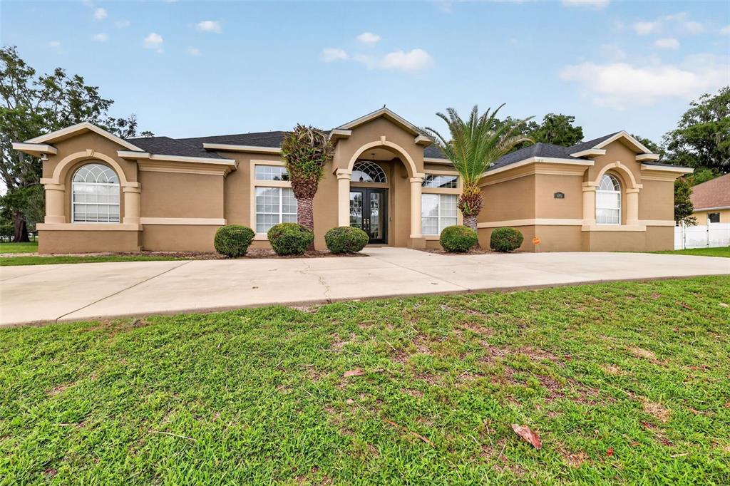 A single-story tan stucco house with a dark roof, arched windows, and a paved driveway — 485 NW 45TH LANE, OCALA, FL
