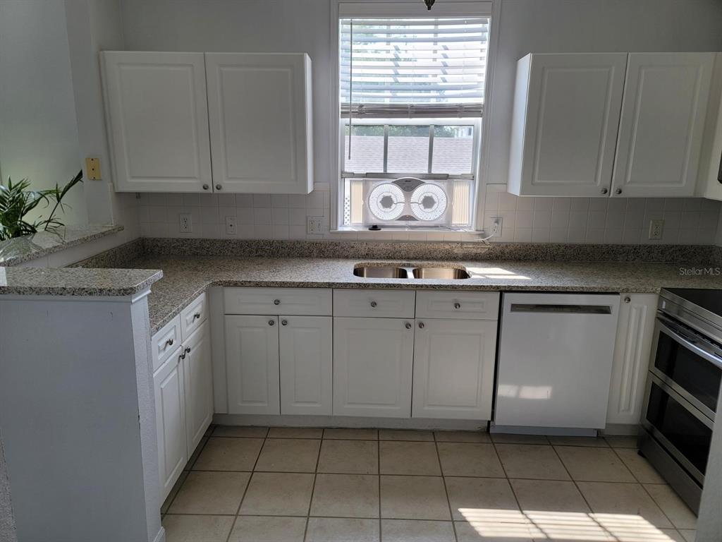 A kitchen features white cabinets, granite countertops, a double sink, and a window air conditioner — 265 GOLDENRAIN DRIVE UNIT 265, CELEBRATION, FL