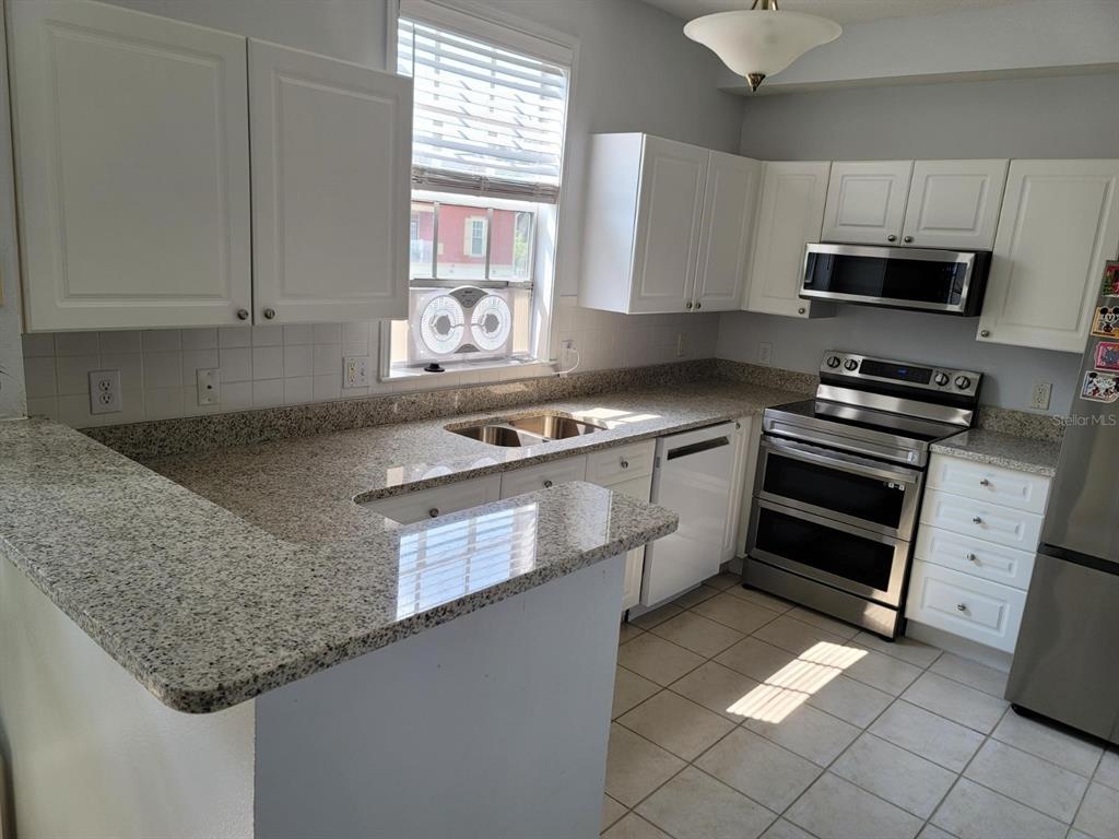 A kitchen with white cabinets, granite countertops, stainless steel appliances, and tile flooring — 265 GOLDENRAIN DRIVE UNIT 265, CELEBRATION, FL