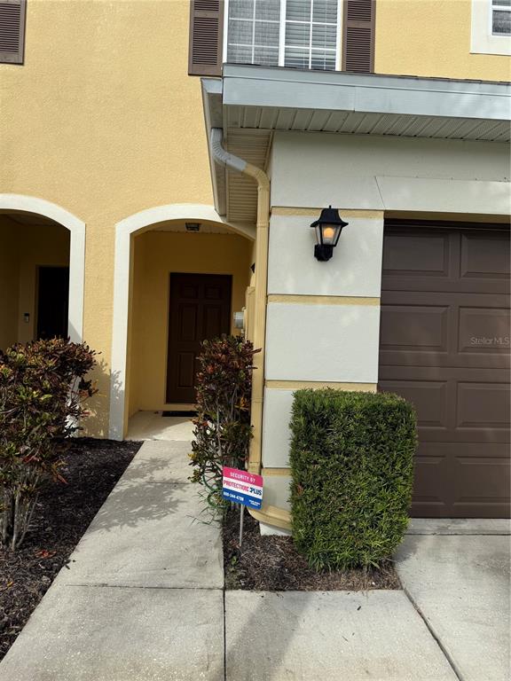 The exterior of a tan townhouse features a brown garage door and a covered entryway — 20460 NEEDLETREE DRIVE, TAMPA, FL