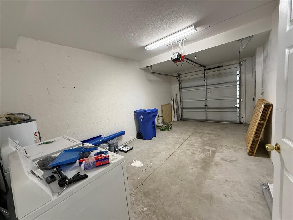 A garage with a concrete floor, white walls, a laundry appliance, and a blue bin — 20460 NEEDLETREE DRIVE, TAMPA, FL