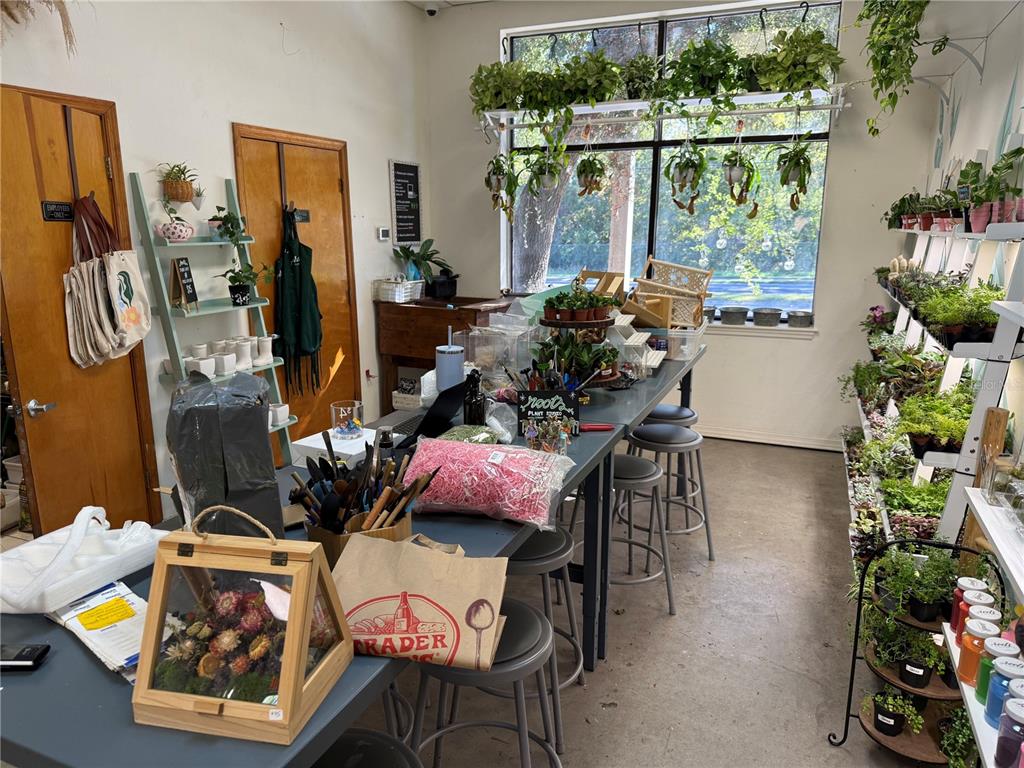 A retail plant shop features a long work table, shelving units, and hanging plants — 4780 NW 39TH AVENUE, GAINESVILLE, FL