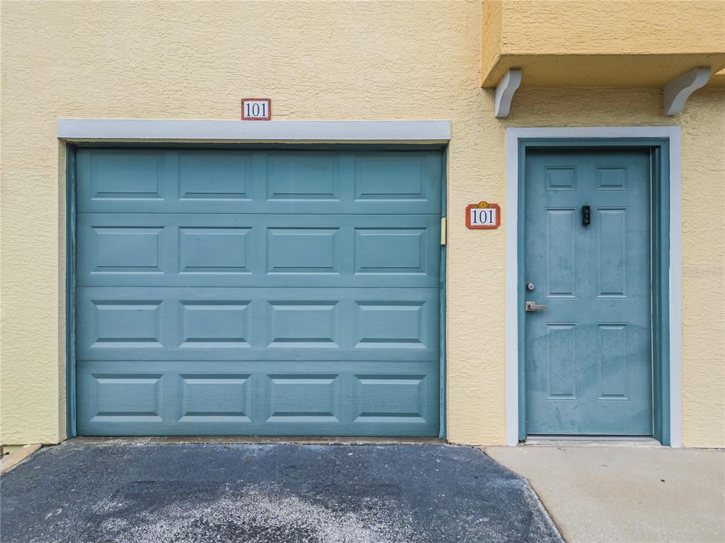 A teal garage door and matching front door are set into a yellow stucco exterior — 12220 WILD IRIS WAY UNIT 101, ORLANDO, FL