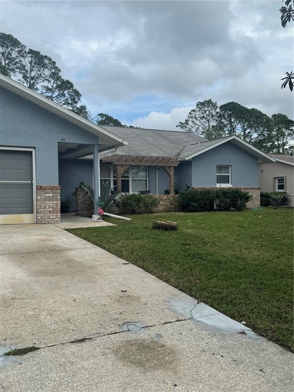 A blue single-story house features a brick facade, a wooden pergola, and a concrete driveway — 180 BEECHWOOD LANE, PALM COAST, FL