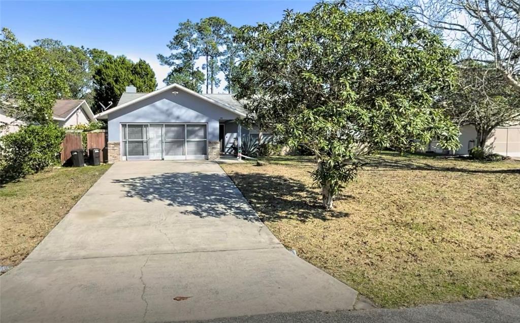A single-story house with a concrete driveway and a large tree in the front yard — 180 BEECHWOOD LANE, PALM COAST, FL
