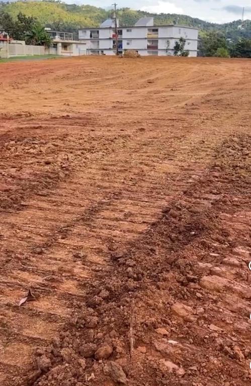 A cleared, graded dirt lot with a multi-story apartment building in the background — BO. QUEBRADA NEGRITO, TRUJILLO ALTO, PR