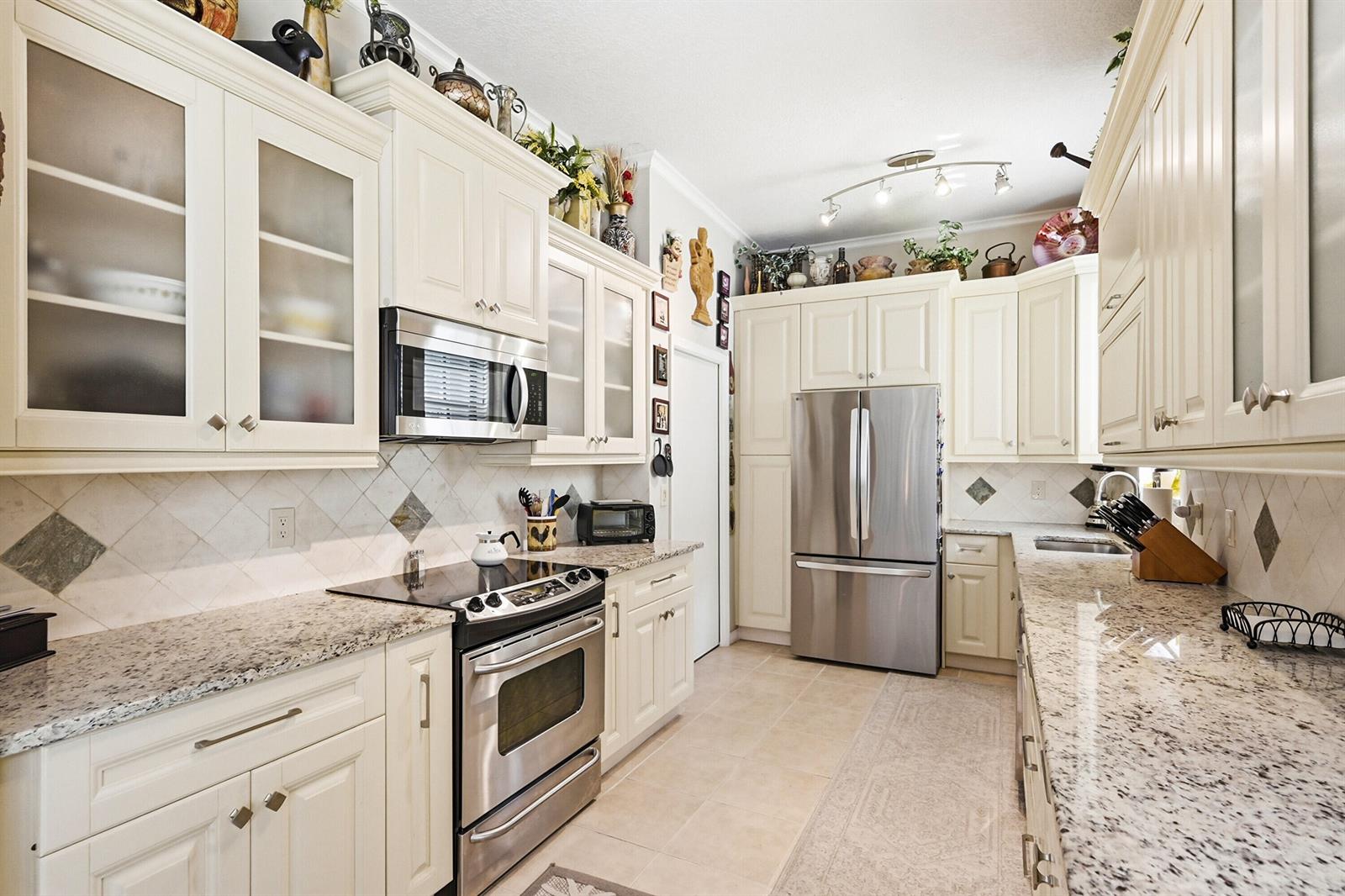 A kitchen features cream-colored cabinets, stainless steel appliances, and speckled granite countertops — 262 Sherwood Forest Drive, Delray Beach FL 33445, DELRAY BEACH, FL