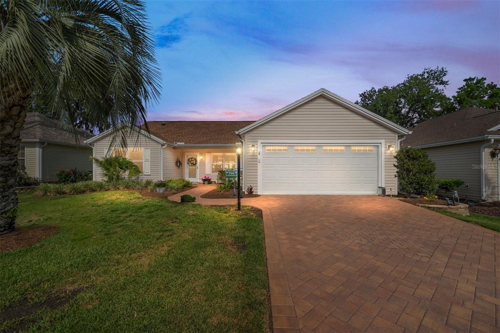 A single-story house with beige siding, a two-car garage, and a brick paver driveway — 9304 SE 170TH HUMPHREYS LOOP, THE VILLAGES, FL