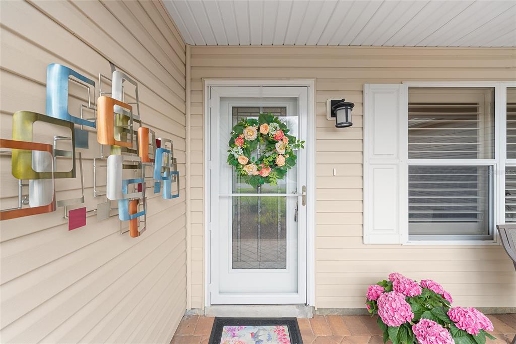 A front porch features beige siding, a white storm door with a wreath, and wall art — 9304 SE 170TH HUMPHREYS LOOP, THE VILLAGES, FL