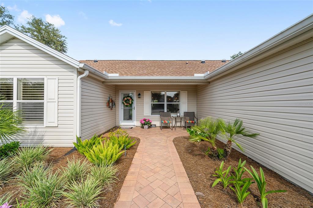 A paved walkway leads to the front entrance of a house with beige vinyl siding — 9304 SE 170TH HUMPHREYS LOOP, THE VILLAGES, FL