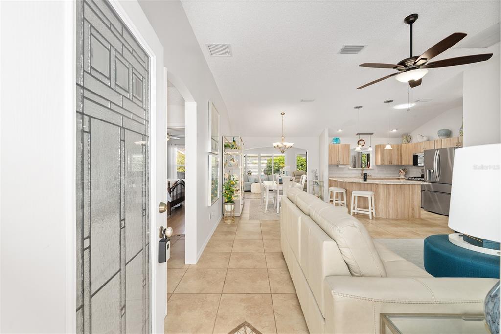 An open-concept living area features tile flooring, a kitchen with light wood cabinets, and furniture — 9304 SE 170TH HUMPHREYS LOOP, THE VILLAGES, FL