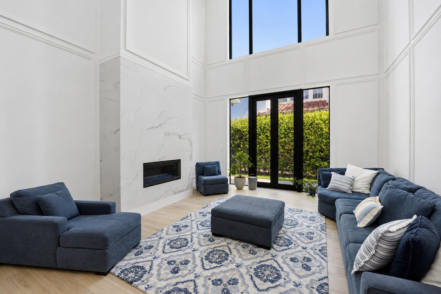 A high-ceilinged living room features a marble fireplace, blue furniture, and large glass doors — 16075 Tuscany Estates Drive, Delray Beach FL 33446, DELRAY BEACH, FL