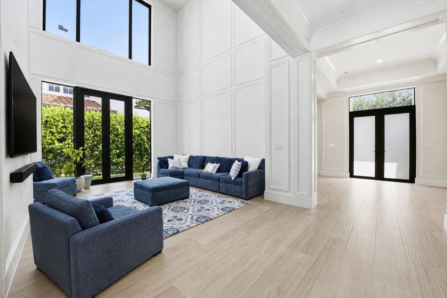 A bright living room with high ceilings, white paneled walls, blue furniture, and light flooring — 16075 Tuscany Estates Drive, Delray Beach FL 33446, DELRAY BEACH, FL