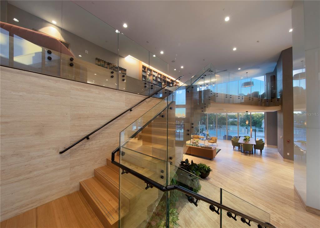 A modern staircase with glass railings overlooks an open-concept living and dining area — 16385 BISCAYNE BOULEVARD UNIT 305, NORTH MIAMI BEACH, FL