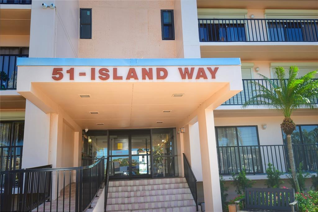 The exterior entrance of a multi-story apartment building features a covered walkway and stairs — 690 ISLAND WAY UNIT 208, CLEARWATER, FL